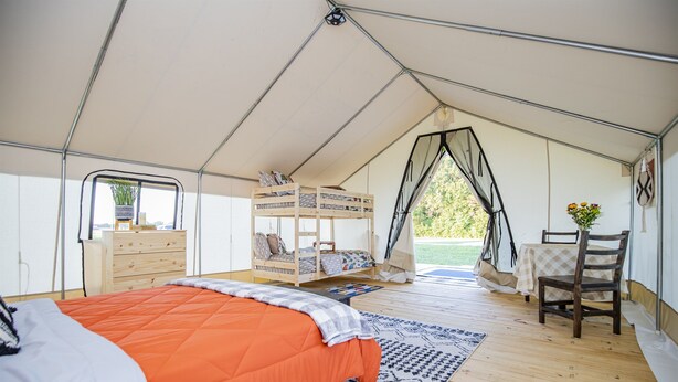 A tented accommodation with a bunk bed, a wooden dresser, a table with chairs, and a view of greenery outside.