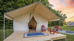 A tented accommodation with a wooden deck, two Adirondack chairs, and a small table.