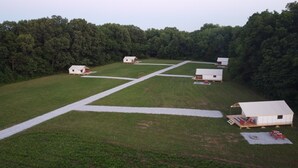 A campground with several small cabins arranged in a grid pattern, surrounded by a forested area.