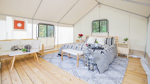 A tented room with a bed, a bench, a small table, and a window.