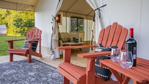 A tented outdoor area with two wooden Adirondack chairs, a table, and a bottle of wine.