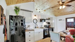 A modern kitchen with white cabinetry, a black refrigerator, a microwave, and a dining area with a red chair and table. - 3 Acres of Luxury and Views in Fred Wine Country! (Fredericksburg)