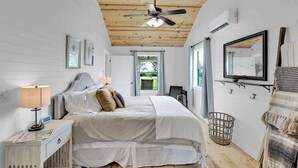 A bedroom with a bed, a bedside table with a lamp, a ceiling fan, a window, and a mirror on the wall. - 3 Acres of Luxury and Views in Fred Wine Country! (Fredericksburg)