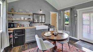 A modern kitchen with grey walls, wooden shelves, and a dining area with a round table and chairs. - 3 Acres of Luxury and Views in Fred Wine Country! (Fredericksburg)