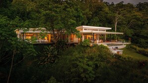 A modern house with a large deck and a swimming pool, surrounded by dense forest. - Modern Luxury with Expansive Ocean View and Covered Patio -Private Waterfall! (Uvita)