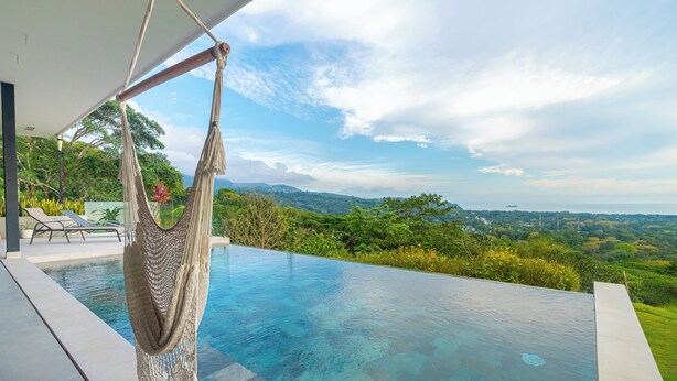 A pool with a hammock, lounge chairs, and a view of a lush landscape. - Modern Luxury with Expansive Ocean View and Covered Patio -Private Waterfall! (Uvita)