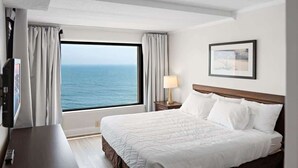 A hotel room with a large window, a bed, a bedside table, a lamp, and a framed picture on the wall. - Oceanfront Condo with Dual Views (Ocean City)