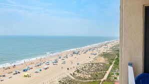A beach with umbrellas and people, a clear sky, and a view of the ocean. - Oceanfront Condo with Dual Views (Ocean City)