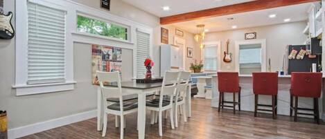 A dining area with a wooden floor, white chairs, and a red bar stool.