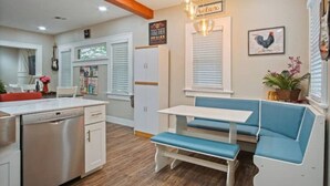A kitchen with a built-in dishwasher, a dining area with a bench, and a wall-mounted light fixture. - Native Inspired, Peaceful, & Practical Home. (Oklahoma City)