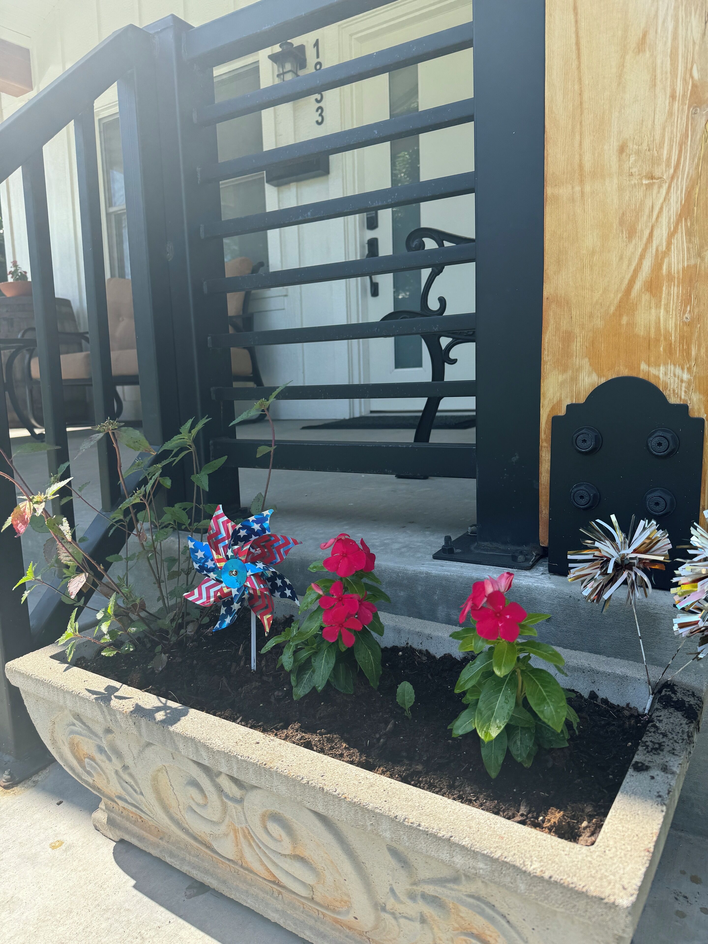 A concrete planter with a decorative design, containing red flowers and a pinwheel.