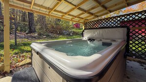 A hot tub under a wooden pergola with a wooden deck and a lattice fence in the background.