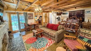 A cozy cabin interior with a wooden ceiling, a sofa with a red blanket, a dining area, and a kitchen.