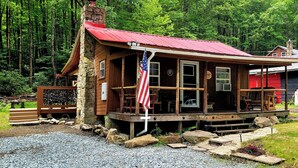 A rustic cabin with a porch, a stone chimney, and an American flag.