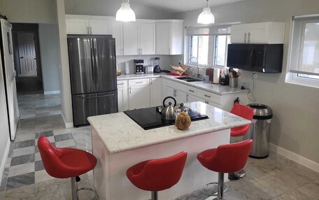 A modern kitchen with white cabinets, a stainless steel refrigerator, a central island with stools, and pendant lighting.