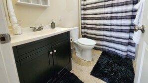 Un baño con lavamanos negro, inodoro blanco y cortina de ducha a rayas.