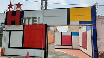 A hotel entrance with a colorful facade, a sign indicating the name, and a security camera.