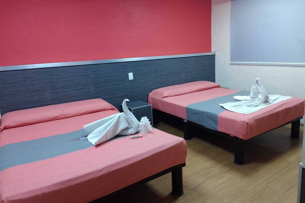 Dos camas individuales con ropa de cama roja y gris, una toalla blanca y una toalla blanca con forma de cisne en cada cama.