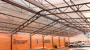 A covered parking area with a metal roof structure and orange walls. There is a sign indicating the parking zone and a notice about parking regulations. - Hotel Piet (Mexico City)