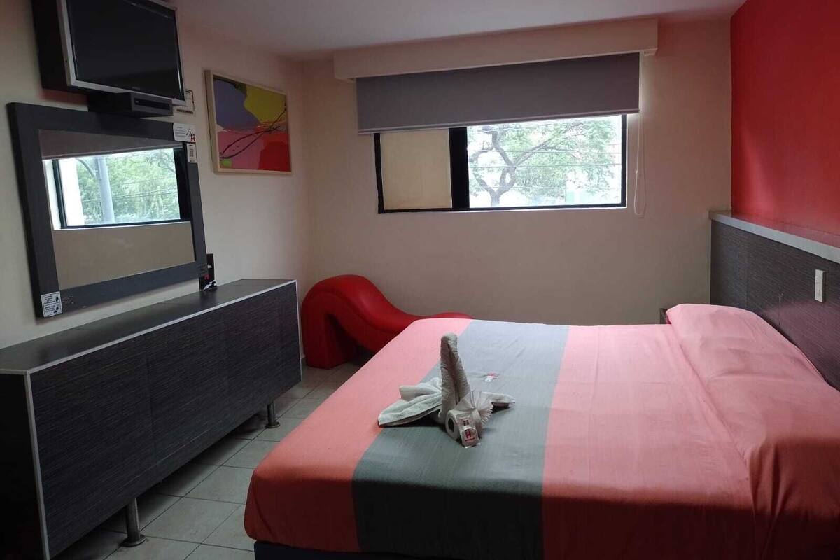 Un dormitorio con cama, cómoda, televisor y ventana.