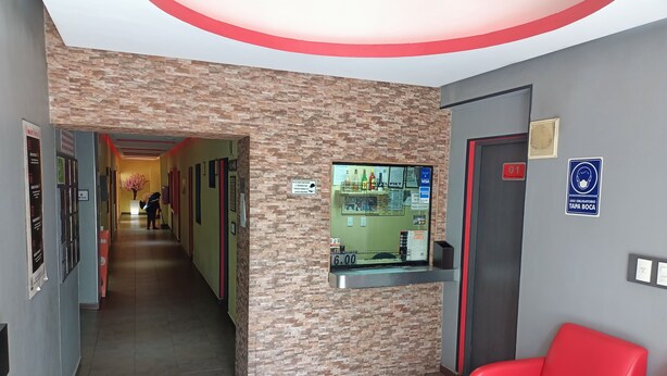 A hotel reception area with a reception desk, a red waiting area, and a hallway leading to other rooms. - Hotel Piet (Mexico City)