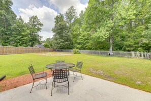A backyard with a round table and four chairs, surrounded by a wooden fence and trees. - Swansboro Vacation Rental, 4 Mi to Hammocks Beach! (Swansboro)