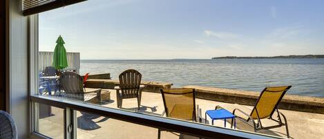 A view from a window overlooking a waterfront patio with outdoor seating and a green umbrella.