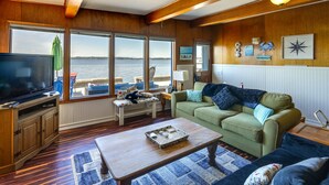 Ein Wohnzimmer mit großem Fernseher, Holzböden, einem grünen Sofa und Blick auf das Wasser.
