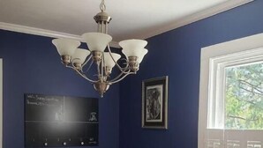 A room with a dining table, two chairs, a chandelier, a framed picture, and a window with shutters.