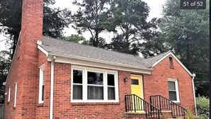 A red brick house with a yellow door, white windows, and a black front porch.