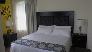 A neatly made bed with a floral bedspread, two bedside tables with lamps, a dark headboard with text, and a window with curtains.
