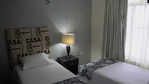 A hotel room with two beds, a nightstand with a lamp, and a window with curtains.