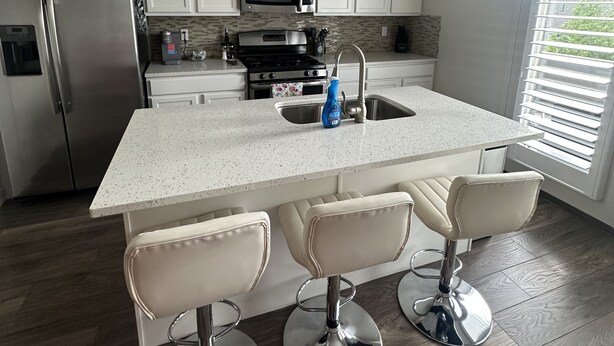 A modern kitchen with white cabinets, stainless steel appliances, a central island with bar stools, and a large window with blinds. - Beautiful Townhouse ! (South Jordan)