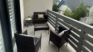 A balcony with wicker furniture, a small table, and a view of neighboring houses. - Beautiful Townhouse ! (South Jordan)