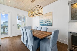 Uma sala de jantar com uma mesa de madeira e cadeiras estofadas em azul claro, um lustre e um quadro na parede.