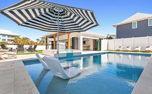 A swimming pool with lounge chairs and a striped umbrella.