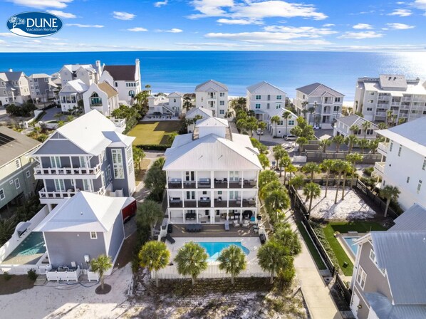 Uma área residencial costeira com várias casas brancas, uma piscina e vista para o oceano.