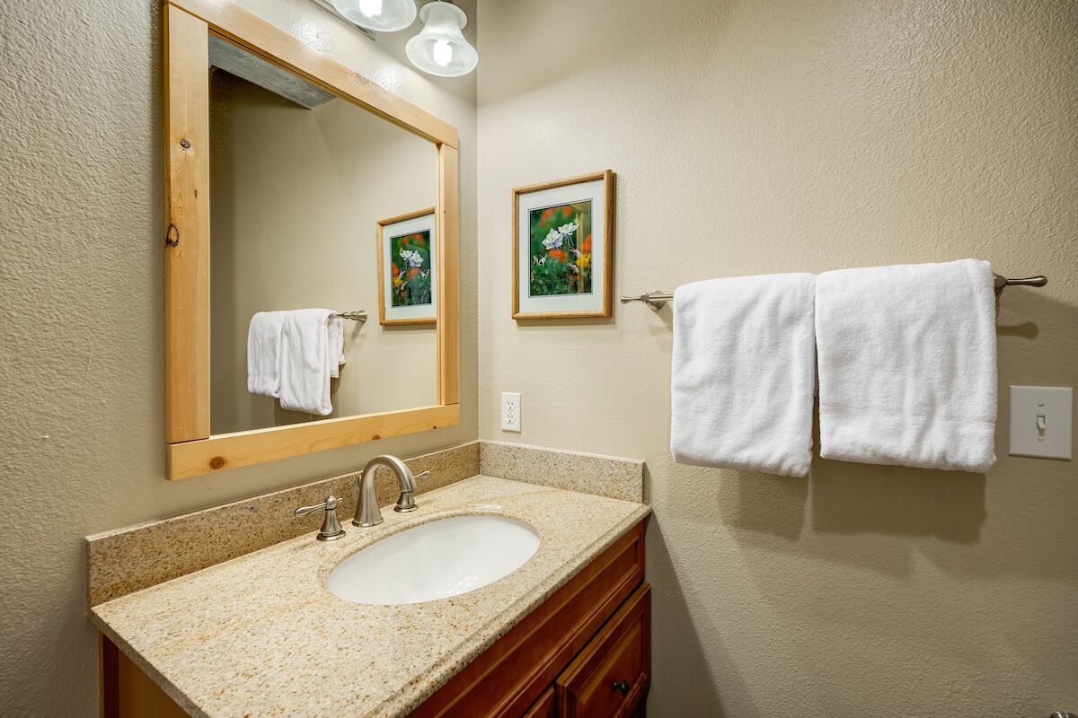 A bathroom with a granite countertop sink, wooden vanity, a large mirror, and two framed pictures on the wall.