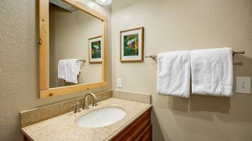 A bathroom with a granite countertop sink, wooden vanity, a large mirror, and two framed pictures on the wall.