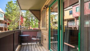 Eine Holzterrasse mit Tisch und Stühlen, eine Schiebetür aus Glas und Blick auf benachbarte Gebäude.