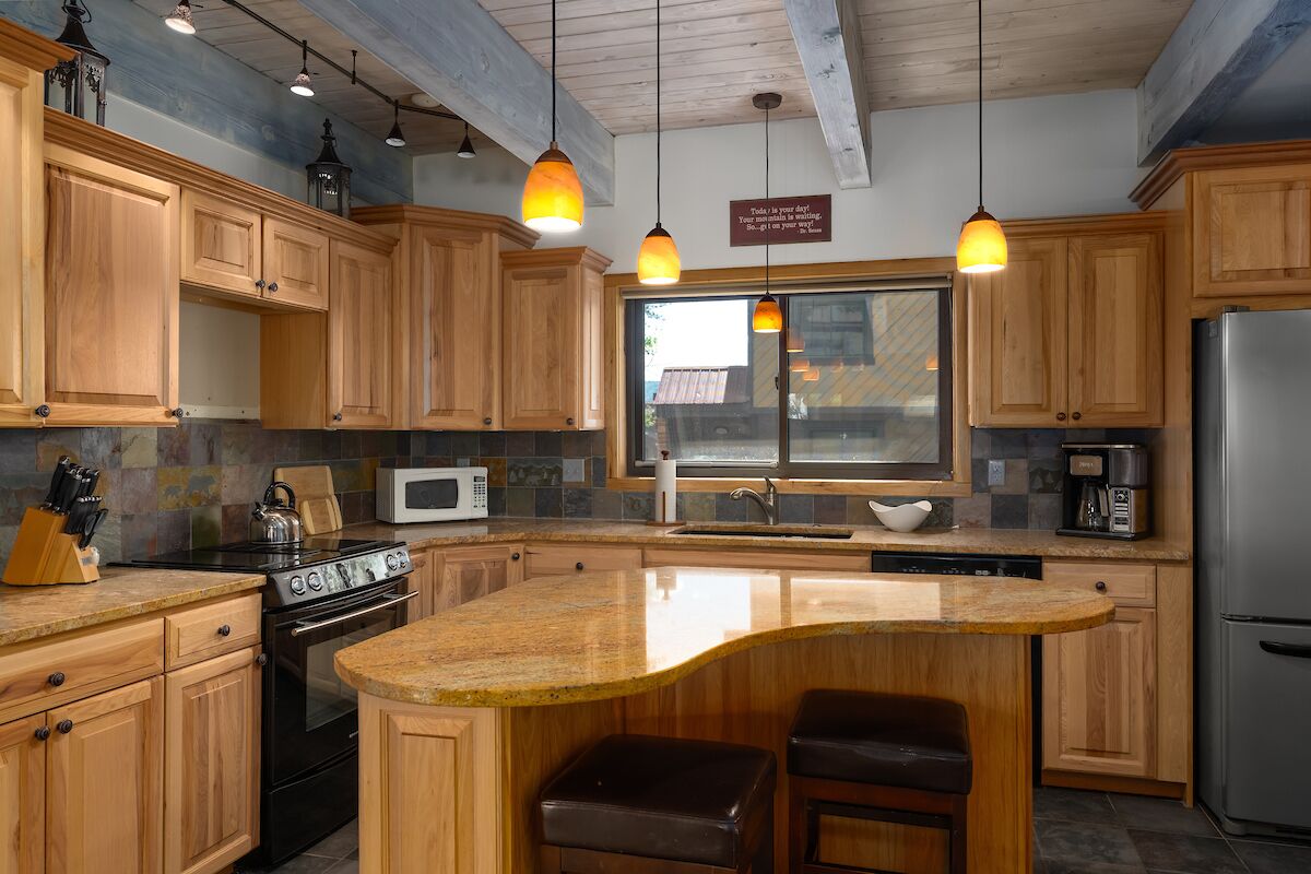 A kitchen with wooden cabinets, a granite countertop, a stainless steel refrigerator, and pendant lighting.