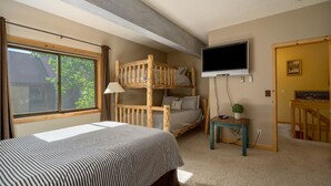 Ein Schlafzimmer mit einem Etagenbett, einem Einzelbett, einem Fernseher und einem kleinen Tisch mit einer Pflanze.
