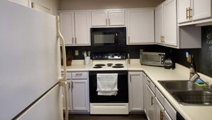A compact kitchen with white cabinets, a black microwave, a stove, and a toaster. - The Redhawk Hideaway: Charming 2BR Condo near Miami Univ in Oxford! Book now! (Oxford)