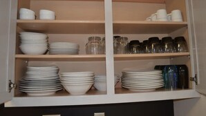 A kitchen cabinet with multiple shelves containing stacks of white plates, bowls, and glassware. - The Redhawk Hideaway: Charming 2BR Condo near Miami Univ in Oxford! Book now! (Oxford)