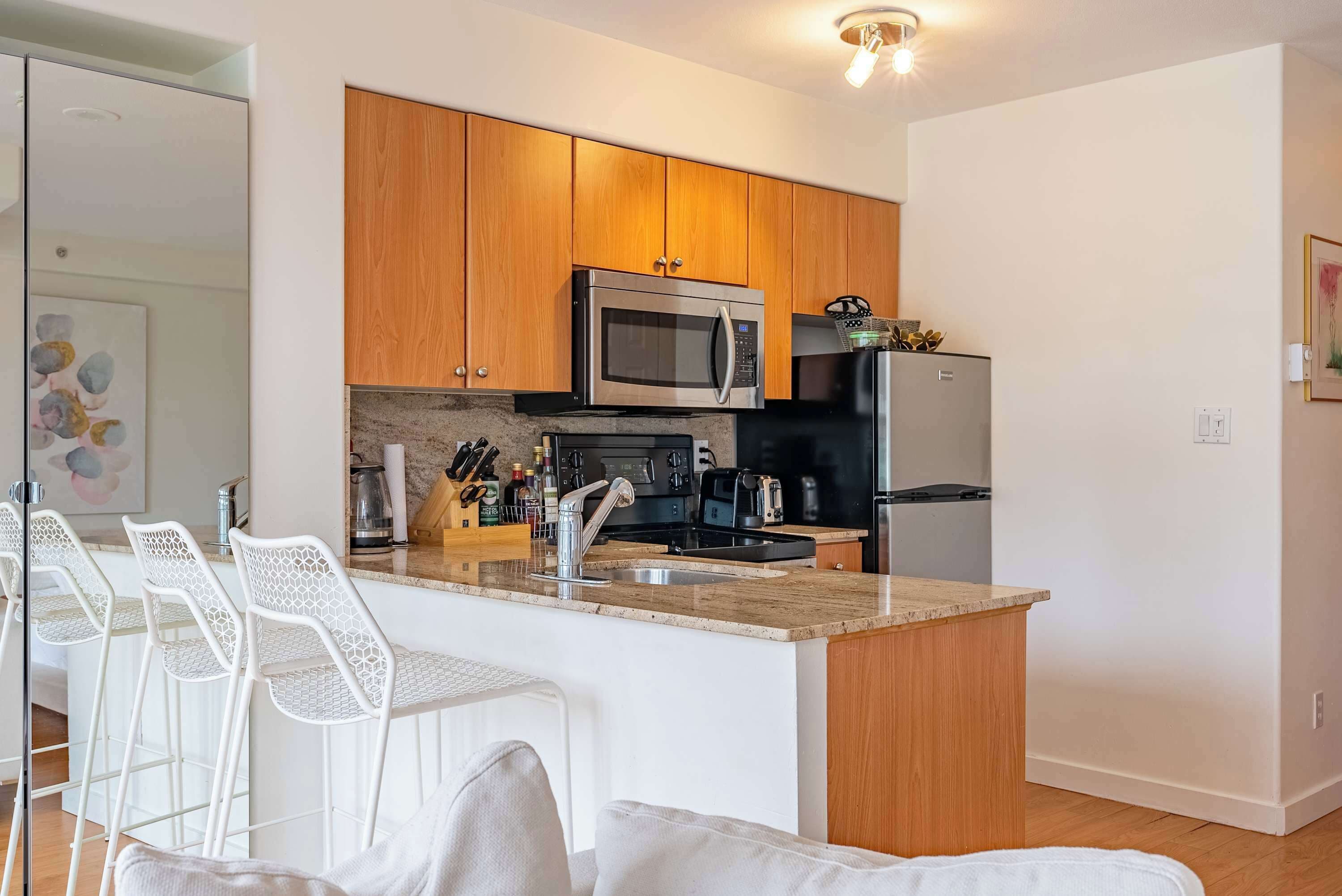 Una cocina moderna con armarios de madera, microondas de acero inoxidable y una isla integrada con taburetes de bar.