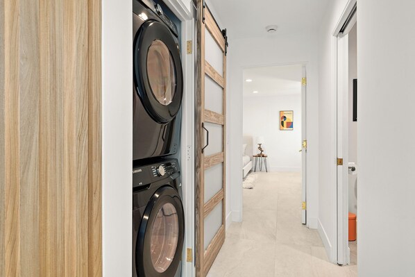 Un couloir au design intérieur moderne, comprenant un lave-linge, une porte en bois et une œuvre d’art encadrée accrochée au mur.