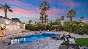 A swimming pool with lounge chairs, a fire pit, and a house with a patio.