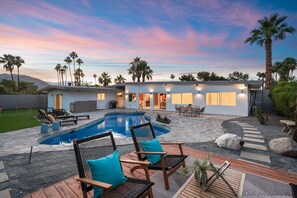 A modern house with a swimming pool, outdoor seating, and a view of palm trees.