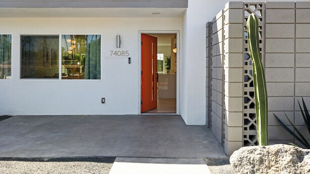A building entrance with a number 74085, a red door, and a cactus plant.