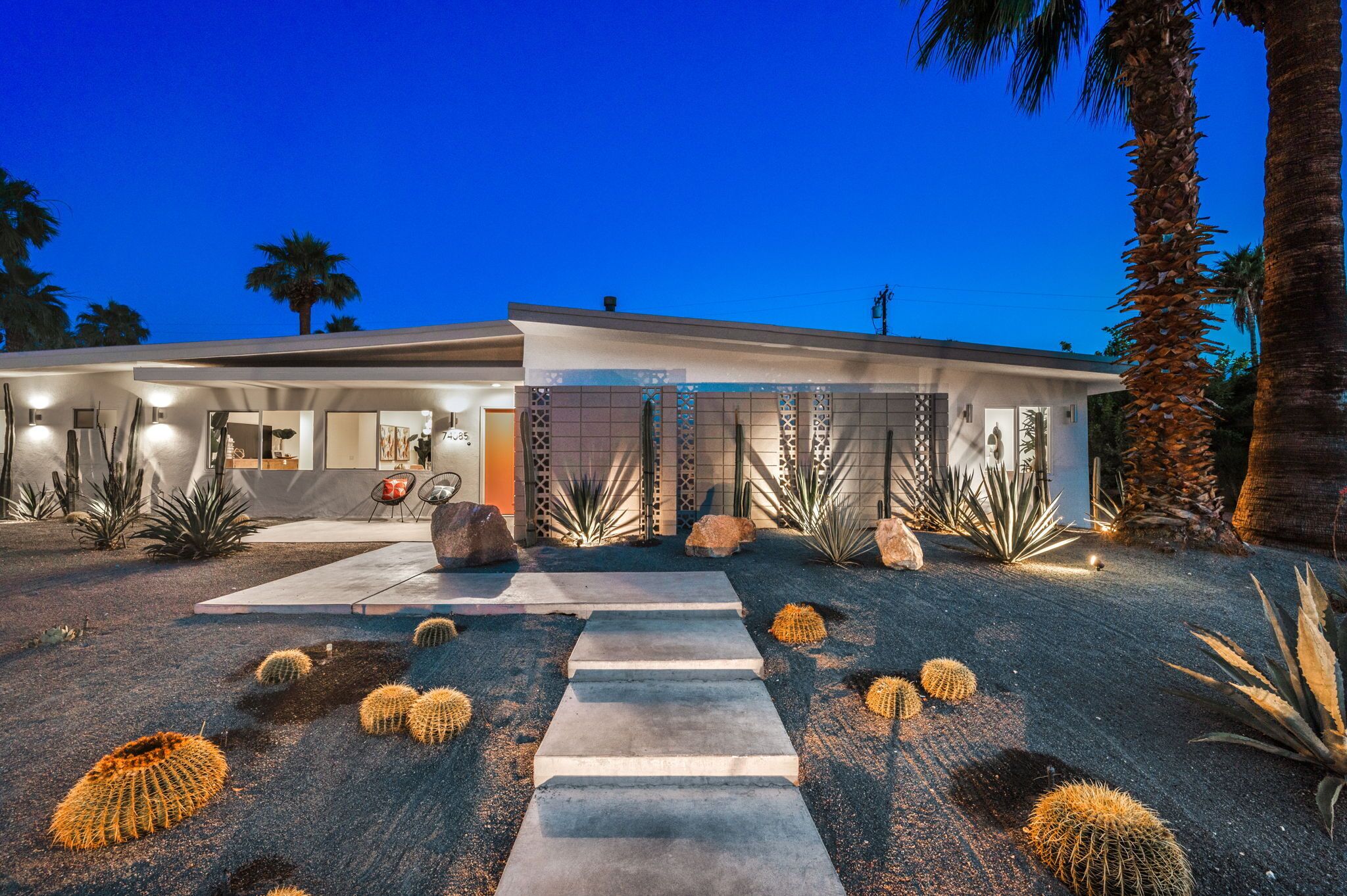 A modern house with a paved driveway, cacti, and palm trees.